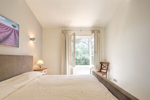 A bedroom with a bed, a nightstand, a lamp, a chair, a window with curtains, and a painting on the wall. - 4 BEDROOM VILLA WITH PRIVATE POOL AND GARDEN (N°443) (La Motte)