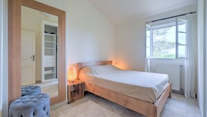Een slaapkamer met een bed, een bedlamp, een spiegel, een kledingkast en een raam met gordijnen.