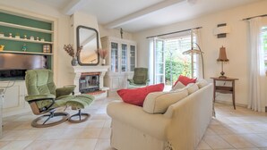 Een woonkamer met een open haard, een groene fauteuil, een beige bank en een grote spiegel.