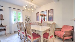 Een eetkamer met een grote tafel, zes stoelen, een kroonluchter en kunstwerken aan de muur.