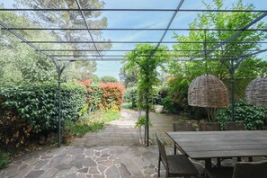 Um pátio externo com piso de pedra, uma mesa de madeira e uma estrutura de pérgola.
