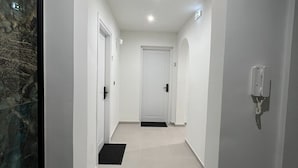 Ein Flur mit weißen Wänden, einer Marmorwand links und einer Tür am Ende.