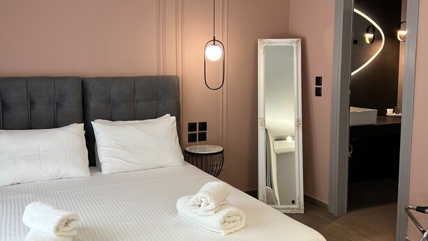 Ein ordentlich bezogenes Bett mit weißen Leinen und Handtüchern, ein großer Spiegel, ein kleiner runder Tisch und eine moderne Lampe.