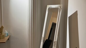 A room with a white column, a mirror on a stand, a wooden shelf with items, and a chair. - Family Suite 1 by Casa Divinus (Athina)