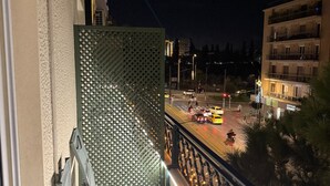 A balcony with a view of a street at night, a patterned wall, and a table with chairs. - Family Suite 1 by Casa Divinus (Athina)