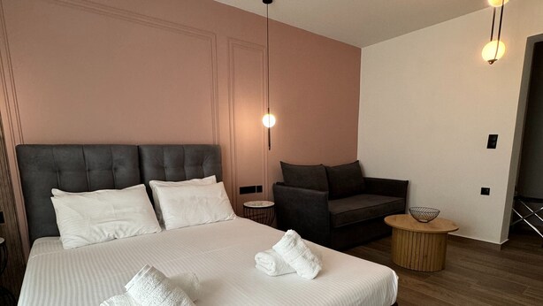 A modern hotel room with a large bed, a sofa, a round wooden side table, and a pendant light. - Family Suite 1 by Casa Divinus (Athina)