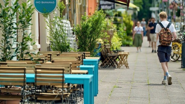 Eine Straße mit Außenbestuhlung, einem Café-Schild und einem Schild mit der Aufschrift 'NO BANANAS'.