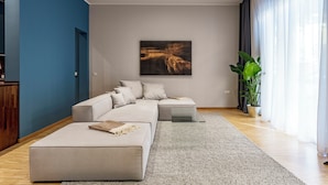 Ein modernes Wohnzimmer mit einem Ecksofa, einem großen abstrakten Gemälde und einer Topfpflanze.