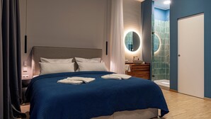 Ein modernes Hotelzimmer mit einem großen Bett, einem Nachttisch, einem Spiegel, einem Badezimmer mit einer blauen Duschkabine und einer Tür.