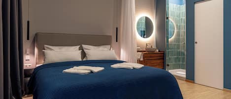 Een moderne hotelkamer met een groot bed, een nachtkastje, een spiegel, een badkamer met een douche met blauwe tegels, en een deur.