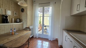 Eine Küche mit Holztisch, einer Kaffeemaschine, einer Uhr und Blick durch eine Glastür auf eine Terrasse.