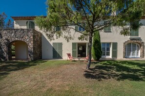 Una casa a due piani con un ingresso ad arco in pietra, un portico coperto con sedie e un prato curato.