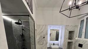 Une salle de bain moderne dotée d’une douche, de toilettes et d’un lavabo, avec un revêtement de sol en marbre et un luminaire au design géométrique.