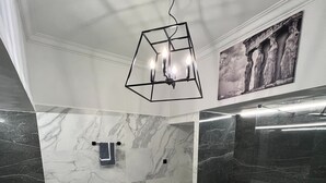 Une salle de bain avec un sol en marbre, un luminaire au design géométrique, un porte-serviettes et une cabine de douche en verre.