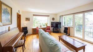 Una sala de estar con un piano, un sofá, un televisor y ventanas amplias.