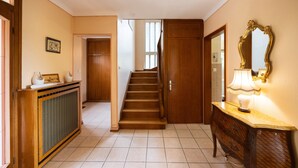 Un pasillo con una escalera de madera, una consola con una lámpara y un espejo en la pared.