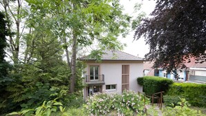 Una casa moderna con balcón, rodeada de abundante follaje y un jardín bien cuidado.