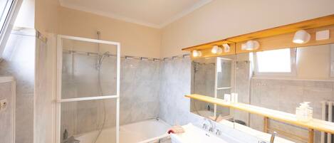 Un baño con ducha de vidrio, bañera, lavamanos doble y espejo con iluminación.
