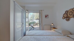 Un dormitorio con cama, mesita de noche, lámpara y vistas al exterior.