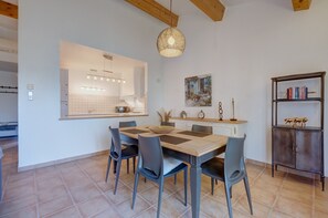 Un coin repas avec une table et des chaises en bois, un luminaire suspendu et une bibliothèque contenant des livres et des objets décoratifs.