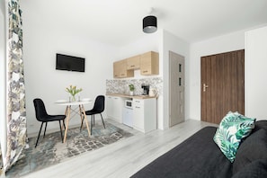 Una cucina moderna con mobili bianchi, un piano di lavoro nero e un forno integrato. C'è una zona pranzo con tavolo e sedie, e un'ampia finestra con vista sulla città.