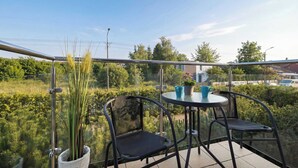 A balcony with a glass railing, two chairs, a small table, and a potted plant. - Cozy Studio close to the Beach | Balcony | Parking (Grzybowo)