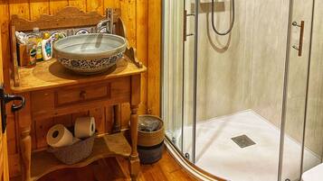 Ein Holzanbau mit Waschbecken, einer Dusche mit Glastür und Holzboden.