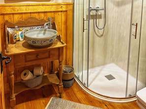 Un tocador de madera con lavabo, una ducha con puerta de vidrio y suelo de madera.