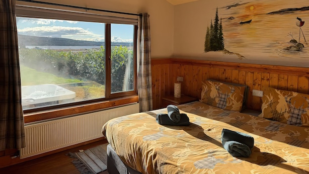 A bedroom with a large window, a bed with a patterned bedspread, a wall mural, and a radiator. - No. 7 (Enniskillen)