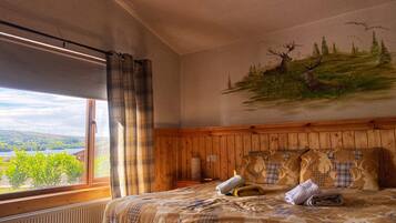 Ein Schlafzimmer mit großem Fenster, einem Bett mit gemustertem Überwurf und einem Wandgemälde von Hirschen.