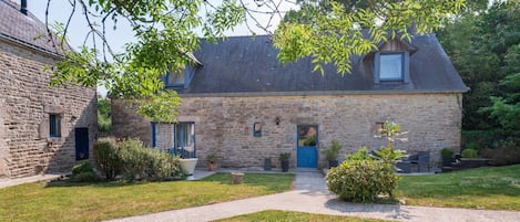 A stone house with a blue door, a paved driveway, and a small garden with potted plants.