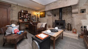 A cozy living room with a stone fireplace, leather furniture, and a bookshelf. - Locmariaquer Guest Room with Terrace, Wi-Fi, and Air Conditioning in High Season (Theix-Noyalo)