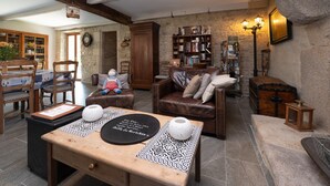 A cozy living room with a wooden table, leather sofa, and a stone wall. - Locmariaquer Guest Room with Terrace, Wi-Fi, and Air Conditioning in High Season (Theix-Noyalo)