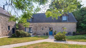 A stone house with a blue door, a paved driveway, and a small garden with potted plants. - Locmariaquer Guest Room with Terrace, Wi-Fi, and Air Conditioning in High Season (Theix-Noyalo)