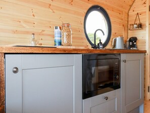 A compact kitchen with a built-in dishwasher, a round window, and a wooden countertop. - Stargaze (Truro)