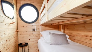 Habitació de cabana de fusta amb lliteres, una finestra de sostre circular i una taula petita negra.
