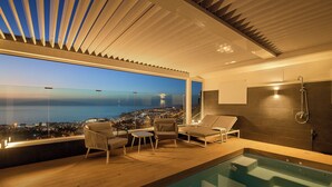 En pool på taget med udsigt over byen i skumringen, et glashuset loungesområde og en moderne bruseplads.