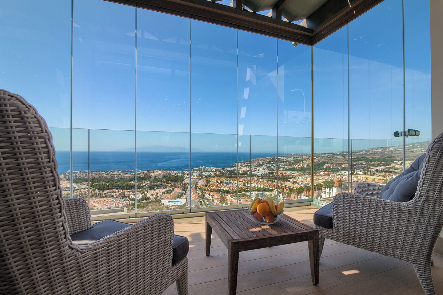 A balcony with wicker chairs, a table with fruit, and a cityscape view.