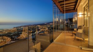 En balkon med gelænder af glas med udsigt over bybilledet i skumringen.
