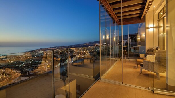 A balcony with a glass railing overlooking a cityscape at dusk. - Villa Lux Calle Francia (Costa Adeje)