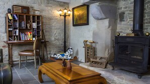 Una habitación con paredes de piedra, una estantería de madera, una mesa con un florero, una silla, un caballo mecedor de madera y una estufa negra.