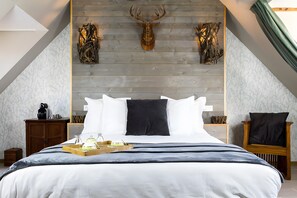A bedroom with a wooden headboard, a bed with white and dark bedding, a bedside table with a lamp, and a chair with a cushion. - Gîte de Calzac Moulin – 3 Bedrooms, Terrace, Unique Decor (Theix-Noyalo)