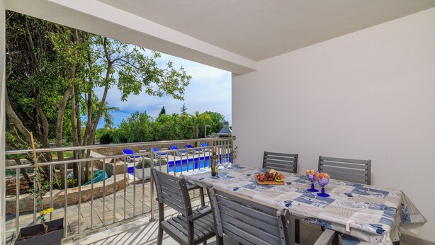 Un balcón con mesa lista para comer, sillas y vistas a árboles y un edificio.