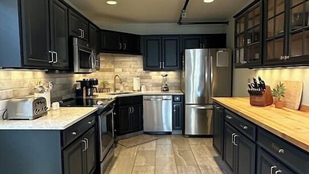 A modern kitchen with dark cabinetry, stainless steel appliances, and a tiled floor. - Two Units, One Stay | Perfect for Groups (Sisters)