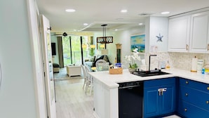A modern kitchen with blue cabinets, a dishwasher, and a dining area with a view. - Island Club 106 | Pool, Hot Tub, Tennis & Beach (Hilton Head Island)