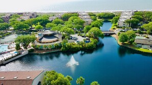 A waterfront property with a central circular building, a swimming pool, and a canal. - Island Club 106 | Pool, Hot Tub, Tennis & Beach (Hilton Head Island)