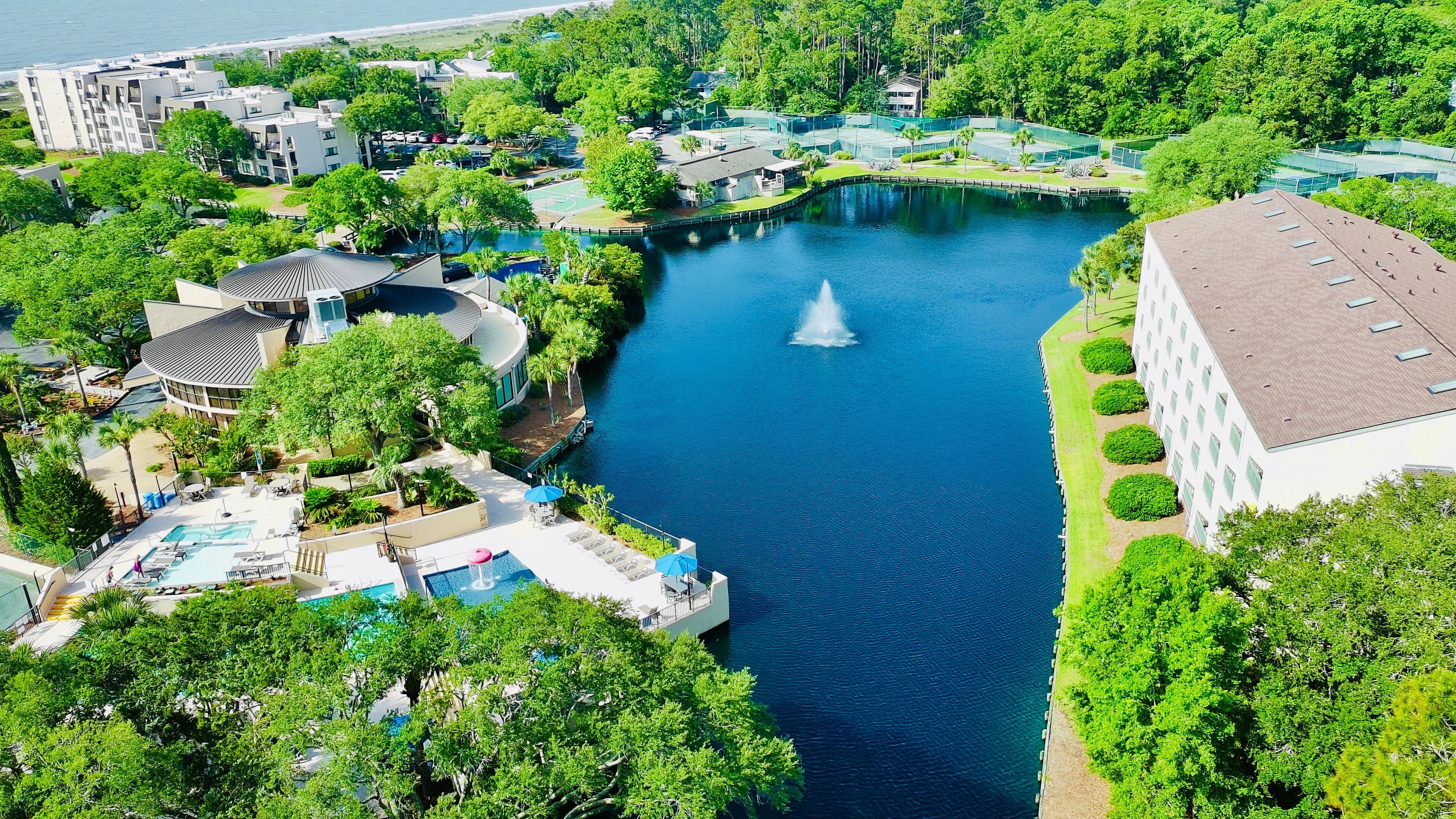 A resort with a central water body, a fountain, and surrounding greenery.