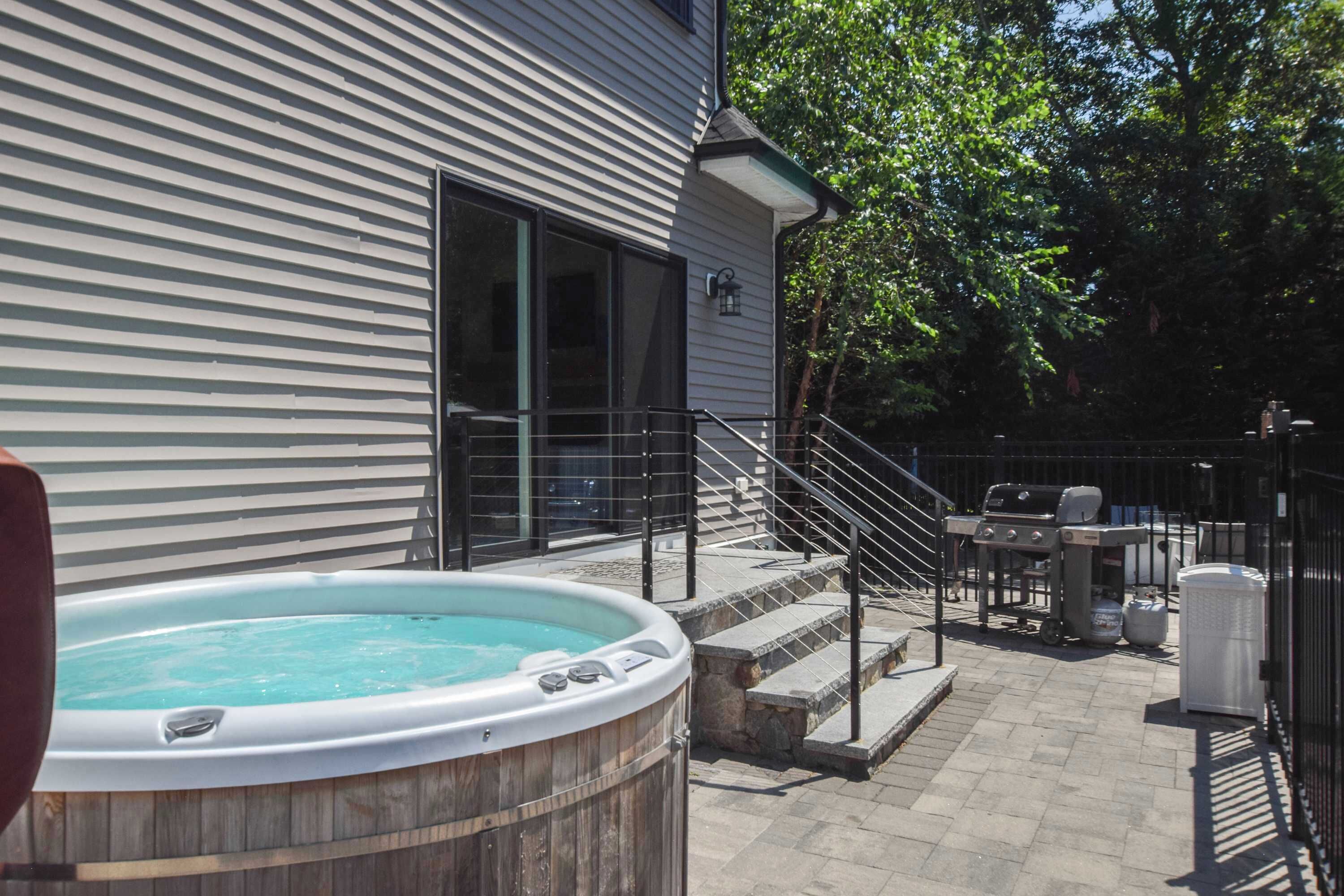 A backyard with a hot tub, outdoor grill, and a staircase leading to a covered patio area.