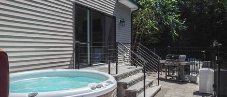A backyard with a hot tub, outdoor grill, and a staircase leading to a covered patio area.