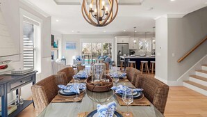 A dining area with a large table, wicker chairs, and a chandelier. - Upscale Beach Retreat w Pool, Half Mile to Beach! (Dennis)